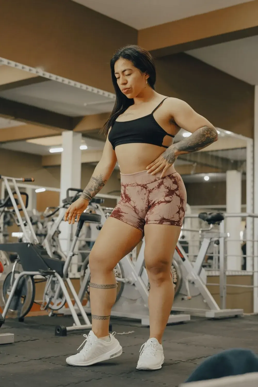 Strong woman with tattoos in gym attire standing confidently indoors.