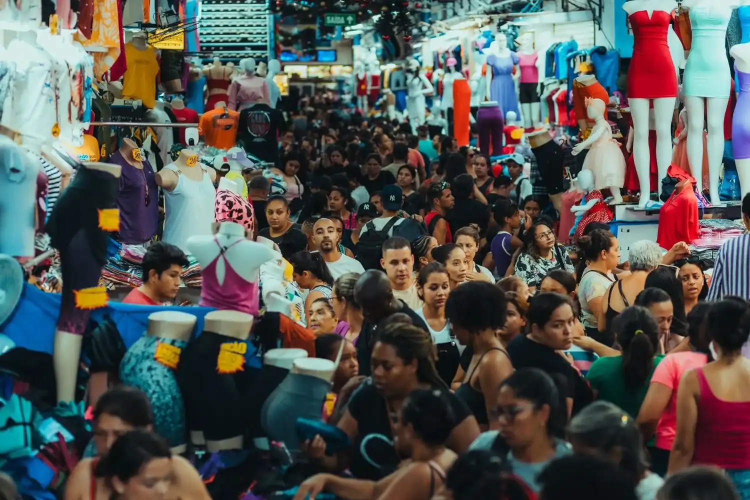 Crowded urban market bustling with people shopping amidst display mannequins.