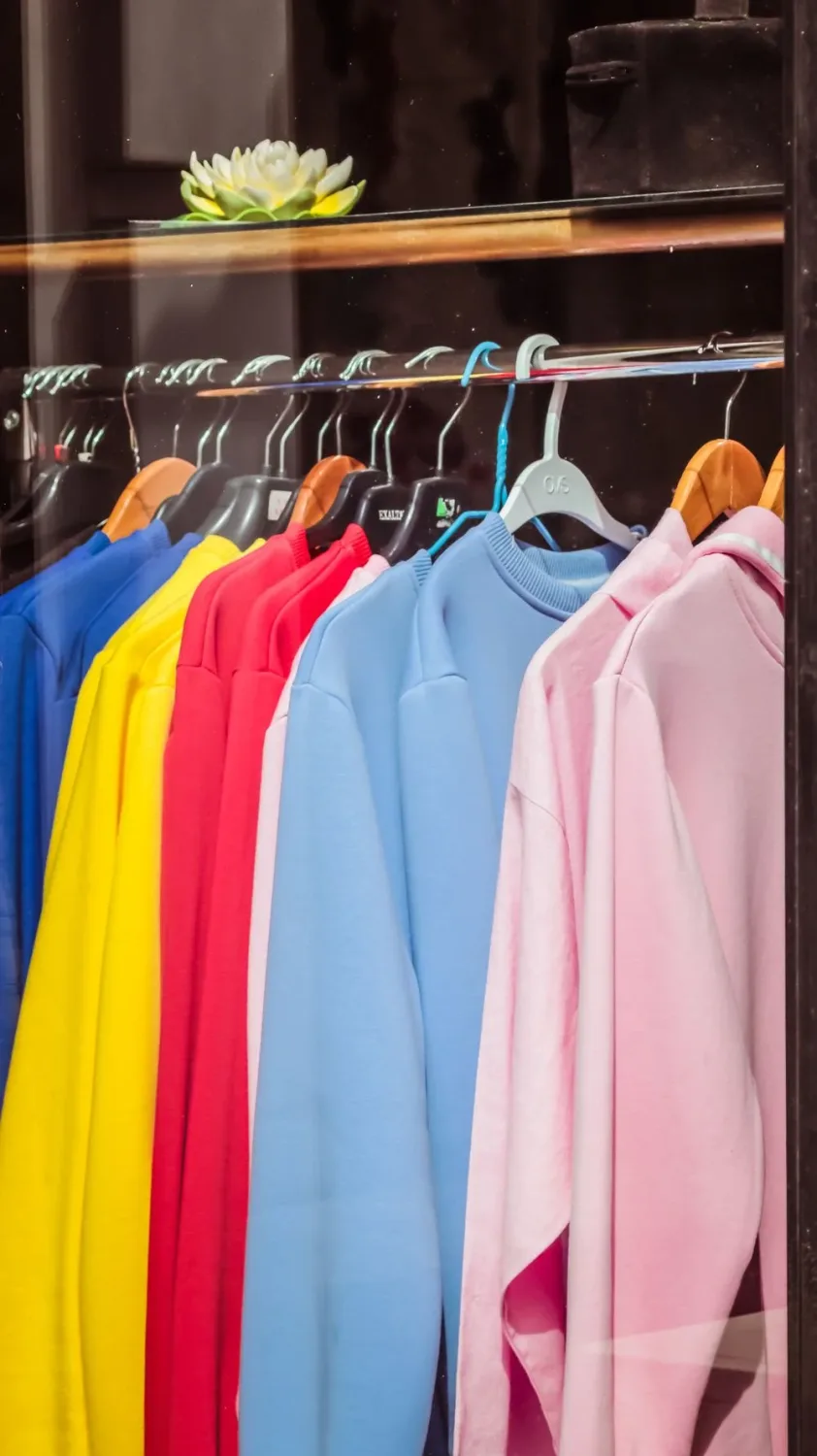 Through glass collection of multicolored sweatshirts hanging on rack on showcase of modern fashion store