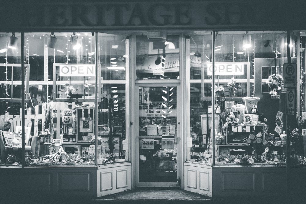 Black and white of store facade with entrance and souvenirs in glass window display located in street in city in evening time